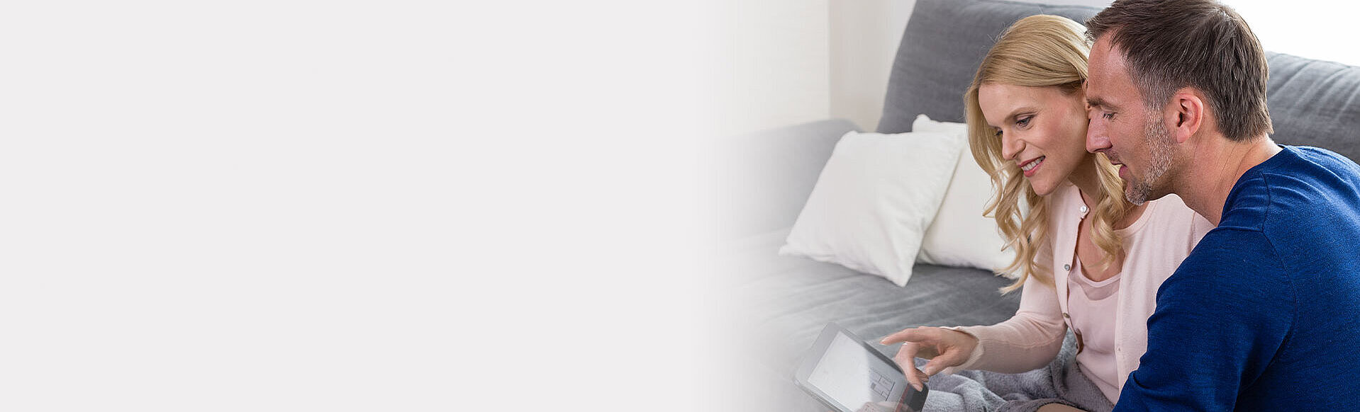 Ein Ehepaar sitzt zu Hause auf dem Sofa und nutzt die Alarmanlagen-App auf seinem Tablet.