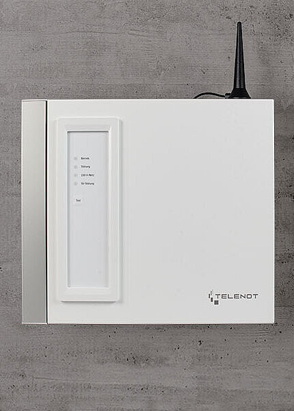 Weißes Gehäuse für Übertragungseinrichtung mit Antenne an grauer Betonwand.