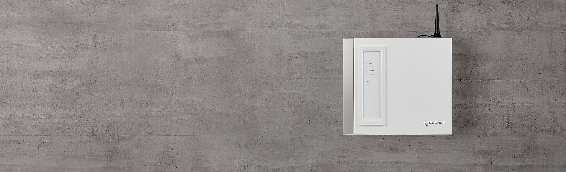 Weißes Gehäuse für Übertragungseinrichtung mit Antenne an grauer Betonwand.