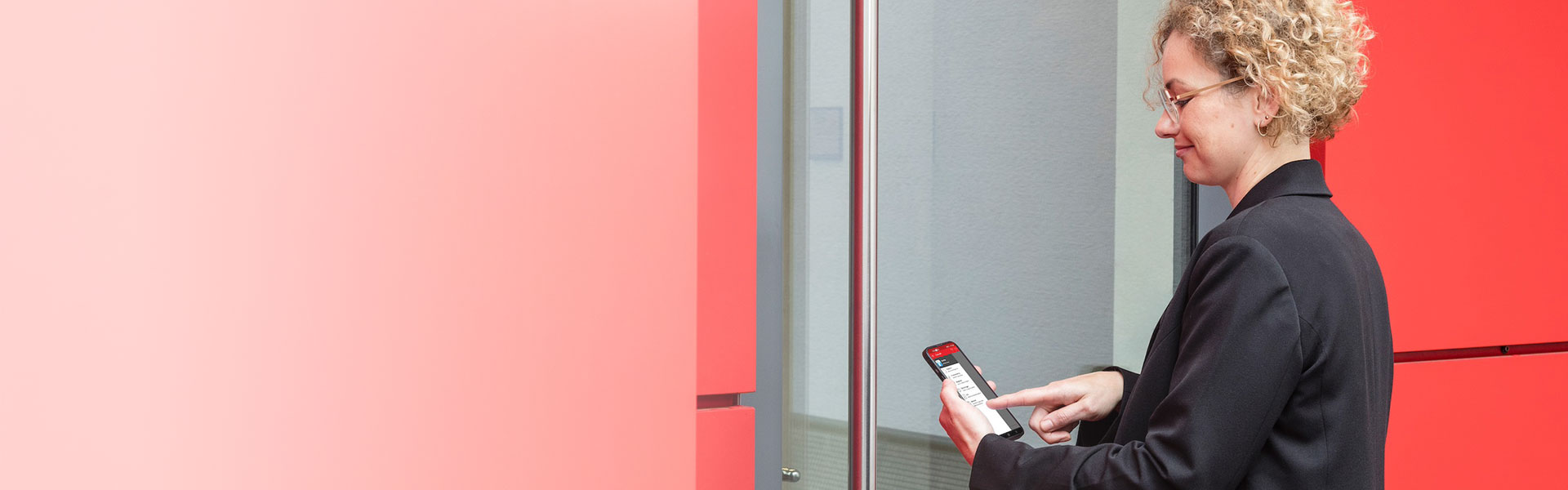 Businessfrau vor der Tür eines Bürogebäudes. Für den Zutritt benutzt sie die App auf dem Smartphone.